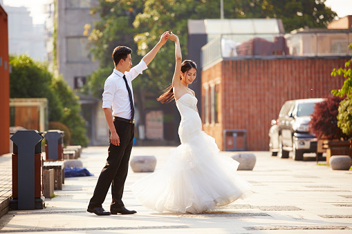 young asian bride and groom in wedding dress dancing in parking lot.