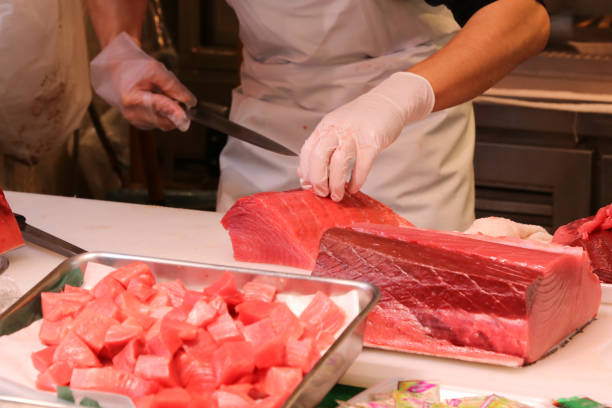 魚屋日本の魚市場で薄くスライスした断片に大きなマグロにナイフを使用します。 - prepared ahi ストックフォトと画像