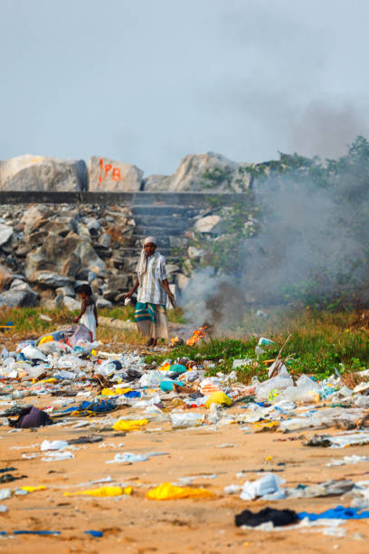 A child girl plays in piles of trash while her mother burns it on the beach of Kollam, Kerala Kollam, India - February 14, 2016: A child girl plays in piles of trash while her mother burns it on the beach of Kollam, Kerala rag picker stock pictures, royalty-free photos & images