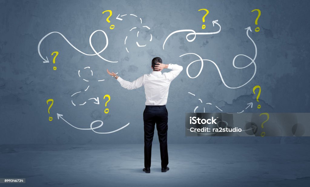 Unsure businessman with question marks A salesman in doubt can not find the solution to the problem concept with curvy lined arrows and question marks drawn on urban wall Lost Stock Photo