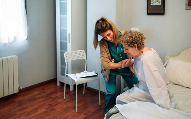 Caregiver helping elderly patient to get out of bed stock photo
