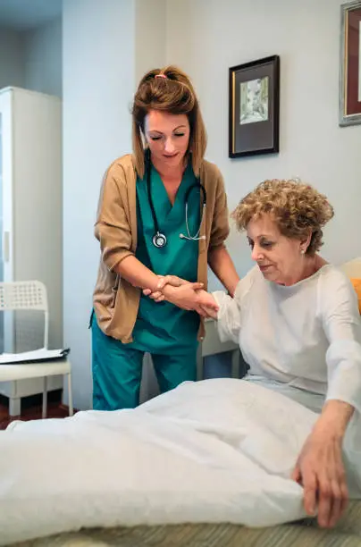 Photo of Caregiver helping elderly patient to get out of bed