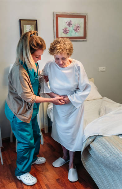 Caregiver helping elderly patient to stand up Female caregiver helping elderly female patient to stand up walking aide stock pictures, royalty-free photos & images