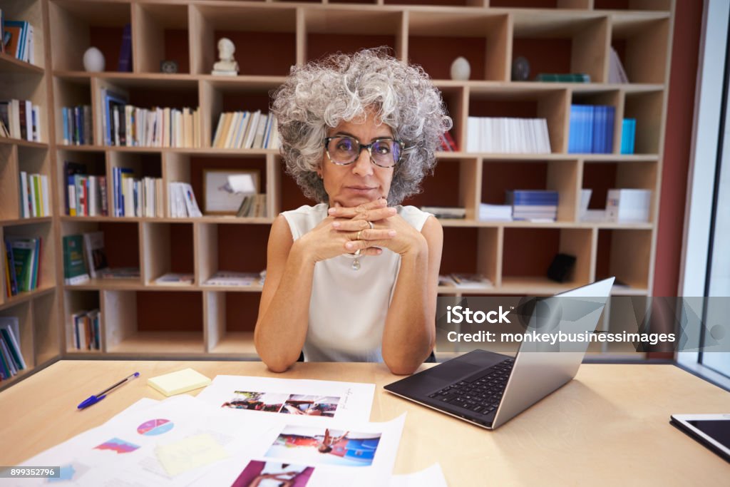 Senior businesswoman using laptop in office looks to camera Desk Stock Photo