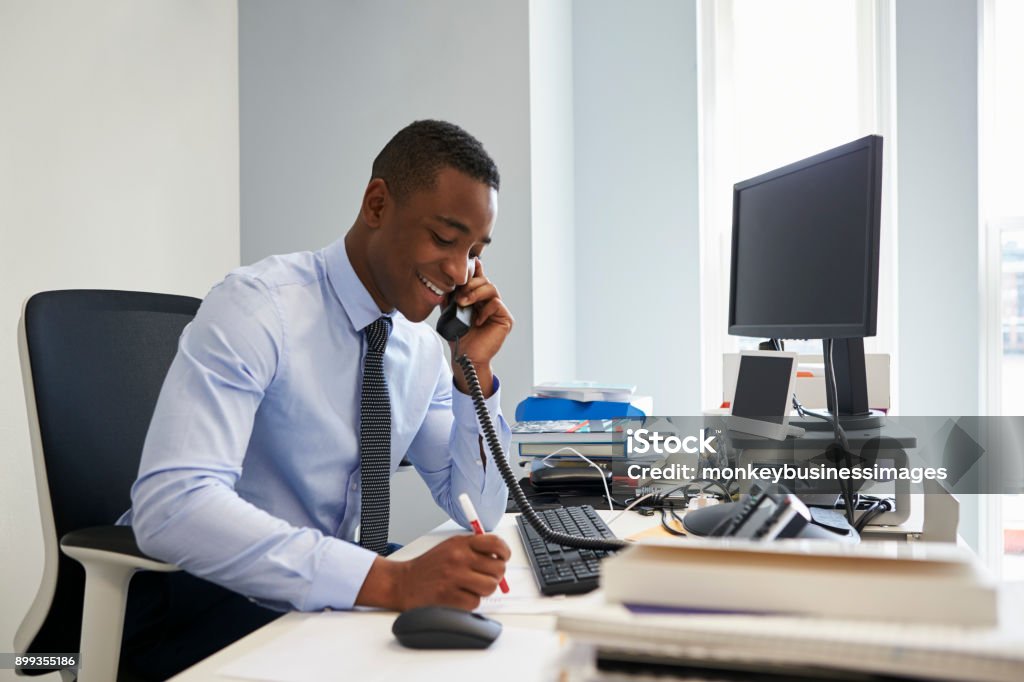 Jeune homme d’affaires noir en utilisant le téléphone sur son bureau - Photo de Bureau - Lieu de travail libre de droits