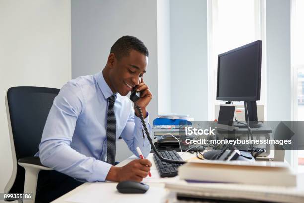 Young Black Businessman Using The Phone At His Office Desk Stock Photo - Download Image Now