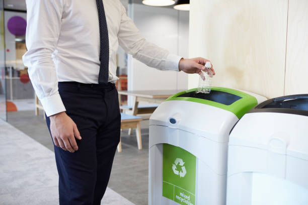 hombre en una oficina lanzando botellas de plástico en contenedor - reciclaje fotografías e imágenes de stock