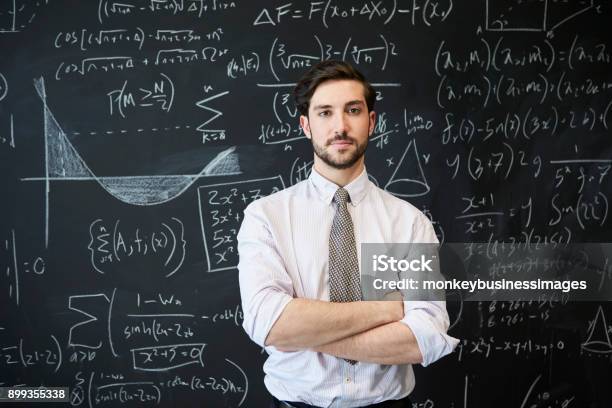 Junger Mann Sucht Kamera Vor Einer Tafel Stockfoto und mehr Bilder von Mathematisches Symbol - Mathematisches Symbol, Mathematik, Lehrkraft