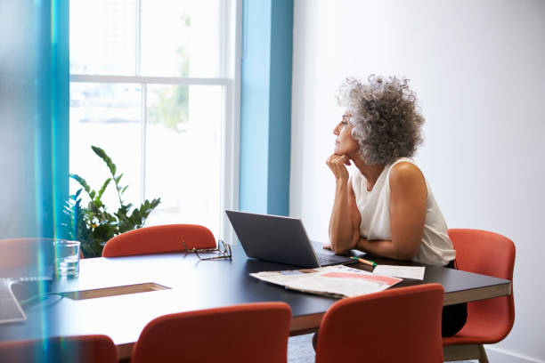 midden leeftijd vrouw kijken uit het raam in de bestuurskamer - woman thinking stockfoto's en -beelden