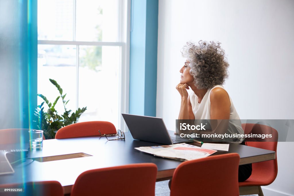 Middle aged woman looking out of the window in the boardroom Contemplation Stock Photo