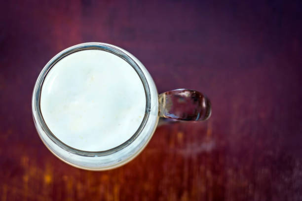 Unsweetened milk in a transparent glass on wooden surface.