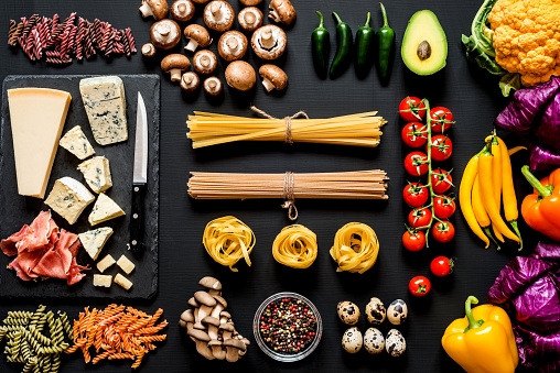 Different fresh ingredients for cooking italian pasta, spaghetti, fettuccine, fusilli and vegetables on a black background. Flat lay, top view