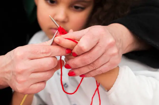 Royalty free stock photo of senior adult teaching little girl how to knit for the first time. Close up on the hands.