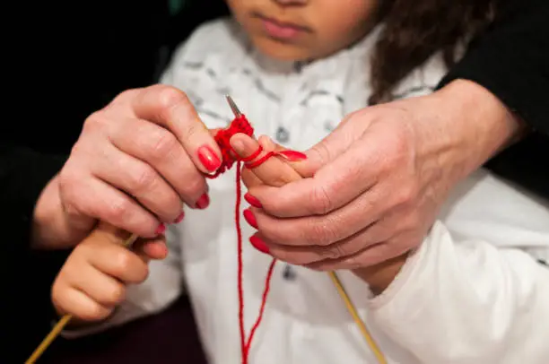 Royalty free stock photo of senior adult teaching little girl how to knit for the first time. Close up on the hands.