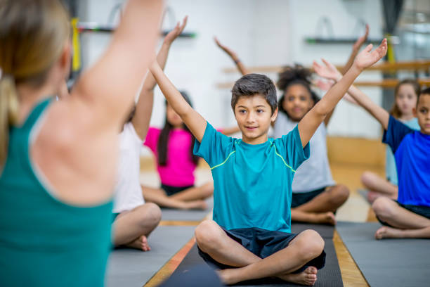 Follow The Teacher A teacher is leading her students during physical education class. She is raising her arms in the air, and her students are following along. They are all wearing casual athletic clothing. physical education stock pictures, royalty-free photos & images