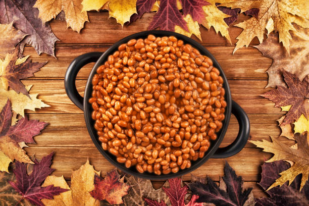Photo of a pot of baked beans. Overhead photo of a pot of baked beans on a wooden table and autumn fall leaves in the background. baked beans stock pictures, royalty-free photos & images