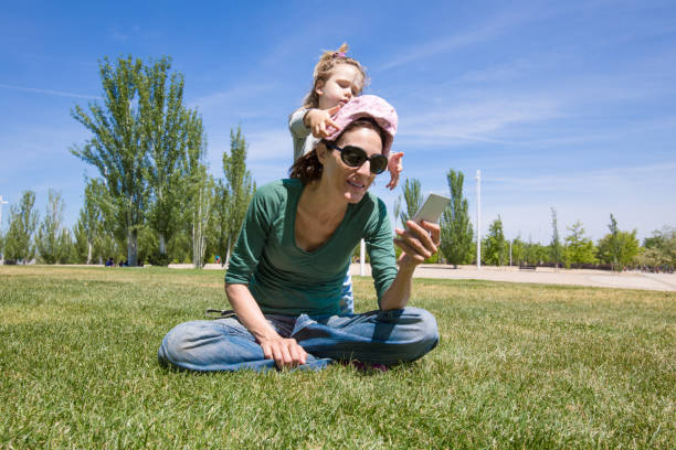 istock child playing with mother reading phone in park 899415466