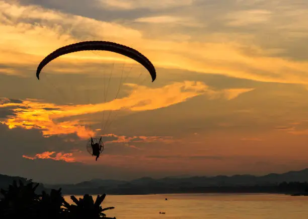 Photo of silhouette flying paramotor over river and sunset sky