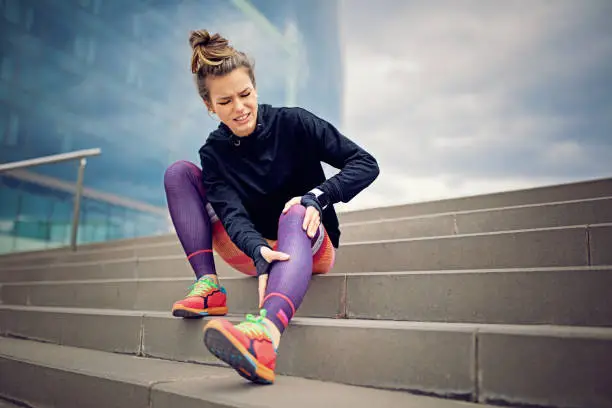 Photo of Injured runner girl is sitting on the city stairs