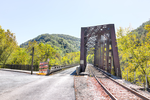 Metal steel covered small railroad bridge in Thurmond, West Virginia with weight limit sign and construction, nobody during autumn fall, highway road