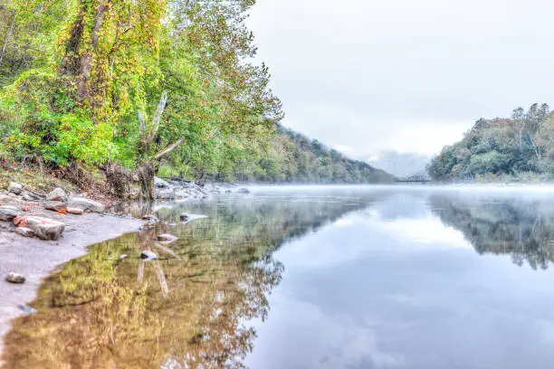 New River Gorge wide canyon water river lake during autumn golden orange foliage in fall by Grandview with peaceful calm tranquil morning bright mist fog