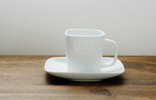 Square white coffee cup and saucer on dark oak table