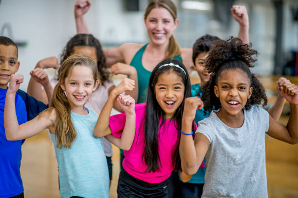 Flexing For The Camera A group of elementary school students are posing with their teacher during gym class. They are all wearing athletic clothing, and flexing for the camera. flexing muscles stock pictures, royalty-free photos & images