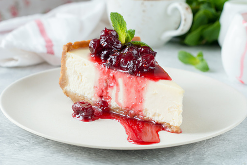 Cheesecake with cranberry sauce and mint leaf on white plate. Delicious New York Cheesecake with berry sauce