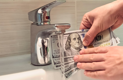 money laundering in washbasin. guy washes the dirty dollars under running water. Male hands holding a hundred dollar bill under water. 500 bucks