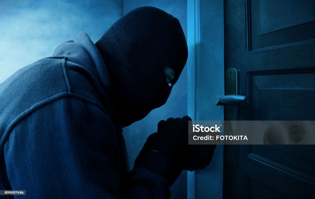 Masked thief using lock picker to open locked door Thief Stock Photo