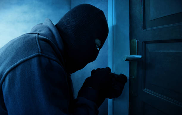 Masked thief using lock picker to open locked door stock photo