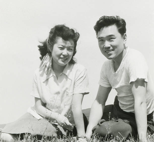 молодая азиатская пара, сидящая на траве - фотографирование фотографии стоковые фото и изображения