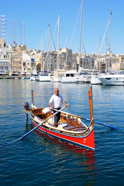 Man steering in Dghajsa, Vittoriosa, Malta. Man steering a traditional Maltese Dghajsa water taxi in the harbour with views towards Senglea waterfront, Vittoriosa, Malta, Europe. coconut crab stock pictures, royalty-free photos & images