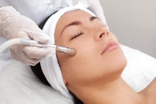 La cosmetóloga hace el procedimiento de microdermoabrasión de la piel del rostro de una mujer joven, hermosa en un salón de belleza photo