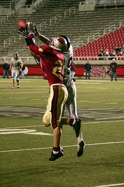 Two American Football Players Jump High to Win Airborne Ball stock photo