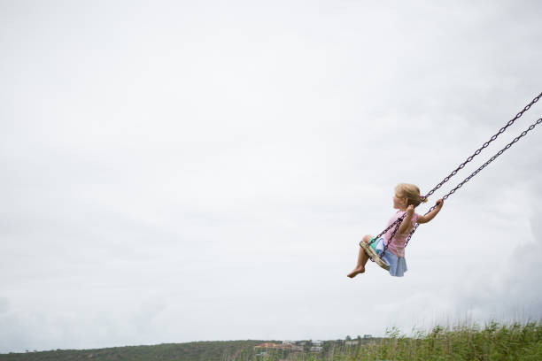 Little child swinging on a wooden swing A little girl swings high on a wooden swing on a cloudy day. innocence stock pictures, royalty-free photos & images