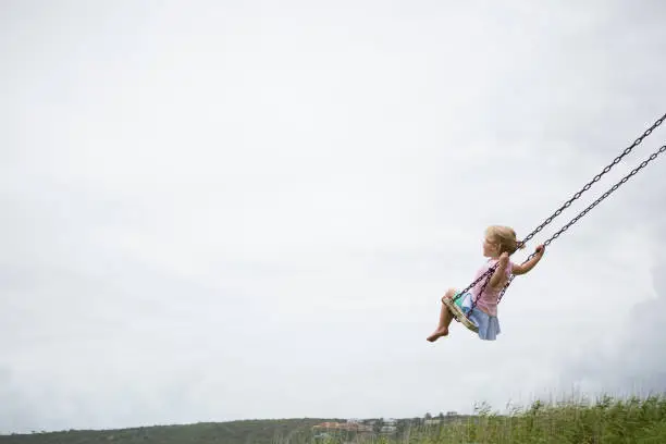Photo of Little child swinging on a wooden swing