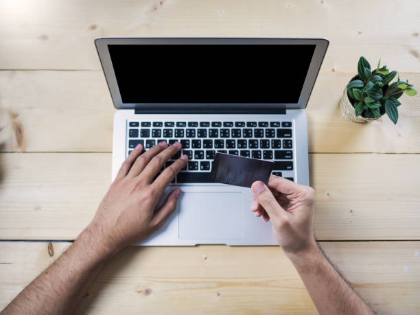 istock Blurred credit card holding by hand with computer notebook, on wooden table, top view 899623648