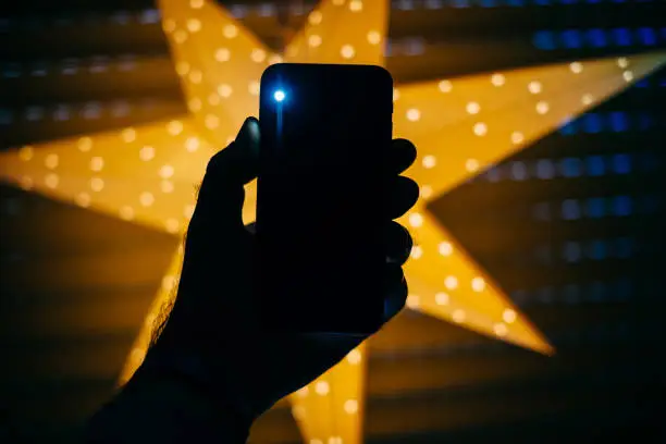 Man holding the new Phone with yellow star Bokeh background featuring a blink light from the rear flash and camera - holiday concept