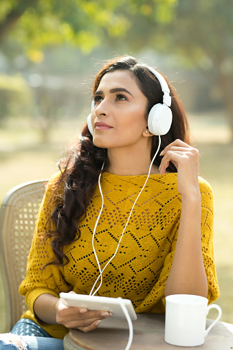 Beautiful Indian woman listening music using digital tablet and headphones at park
