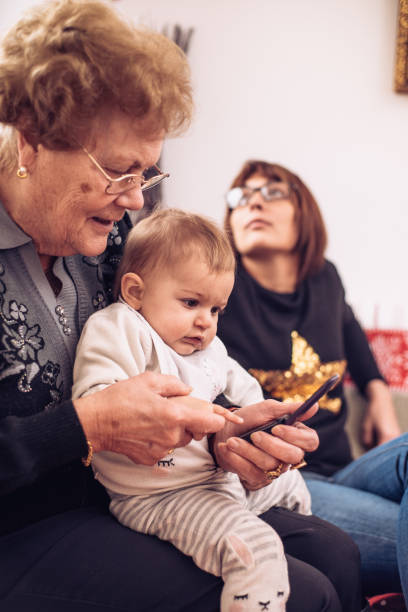 petite fille avec sa mère et la grand-mère en regardant la photo sur l’appareil mobile - generation gap multi generation family vertical holding hands photos et images de collection