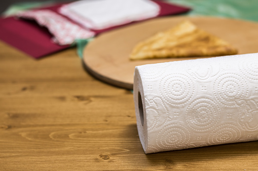 Roll of paper towel on a wooden table with blurred portion of crepe and red table mat.