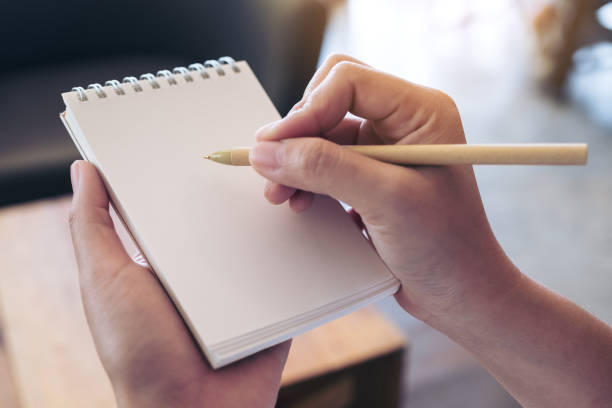 istock Closeup image of a hand holding and writing on a blank white notebook in office 899688542