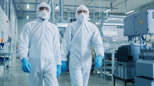 Two Engineers/ Scientists in Hazmat Sterile Suits Walking Through Technologically Advanced Factory/ Laboratory. Clean High-Tech Environment with CNC Machinery. Two Engineers/ Scientists in Hazmat Sterile Suits Walking Through Technologically Advanced Factory/ Laboratory. Clean High-Tech Environment with CNC Machinery. facilities protection services stock pictures, royalty-free photos & images