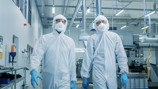 Dos ingenieros / científicos en materiales peligrosos estéril trajes caminando por fábrica tecnológicamente avanzada / laboratorio. Limpiar el ambiente de alta tecnología con maquinaria CNC. photo