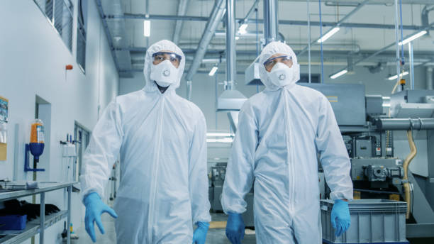 Two Engineers/ Scientists in Hazmat Sterile Suits Walking Through Technologically Advanced Factory/ Laboratory. Clean High-Tech Environment with CNC Machinery. Two Engineers/ Scientists in Hazmat Sterile Suits Walking Through Technologically Advanced Factory/ Laboratory. Clean High-Tech Environment with CNC Machinery. cleanroom stock pictures, royalty-free photos & images