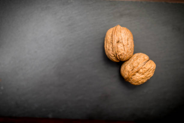 Close up of two walnuts on a black slate background, testicle concept could be used for a testicular cancer advert Close up of two walnuts on a black slate background, testicle concept could be used for a testicular cancer advert testis stock pictures, royalty-free photos & images