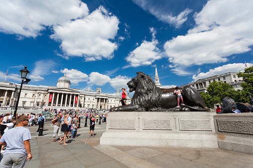 LONDON - AUGUST 20: Lion statue at Trafalgar Square in London with blue sky and tourists passing by on August 20, 2013
