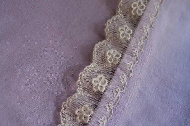 Photo of Ribbon of ivory lace sewn to mauve fabric