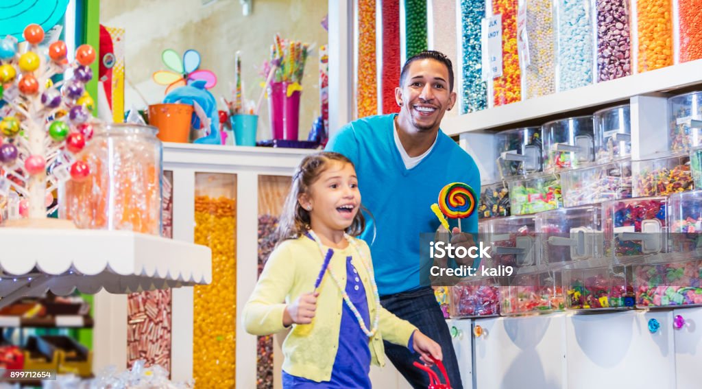 Girl and father in candy store A little 7 year old girl smiling with her father, standing in a candy store, surrounded by jars, containers and displays of colorful candies. They are mixed race Hispanic and Caucasian. Candy Store Stock Photo